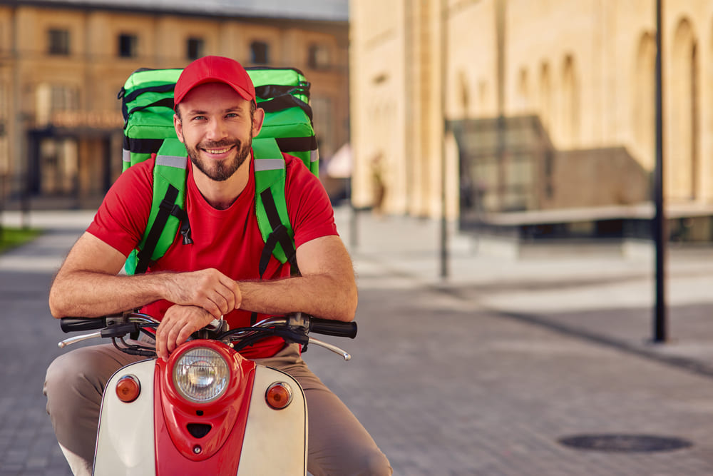 hombre con una mochila de delivery en la espalda sobre una moto estacionada