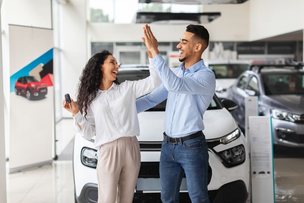 hombre y mujer chocando las manos manifestando alegría por comprar un auto