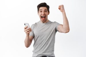Happy man holds smartphone and celebrating, winning online prize, shouts yes and rejoicing, triumphing from success, looks satisfied, white background.