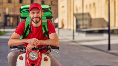 hombre con una mochila de delivery en la espalda sobre una moto estacionada