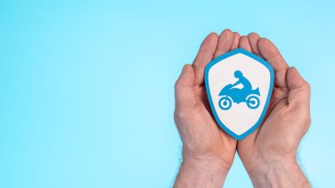 Dos manos sobre un fondo celeste con una imagen de un escudo blanco que tiene una moto en el centro