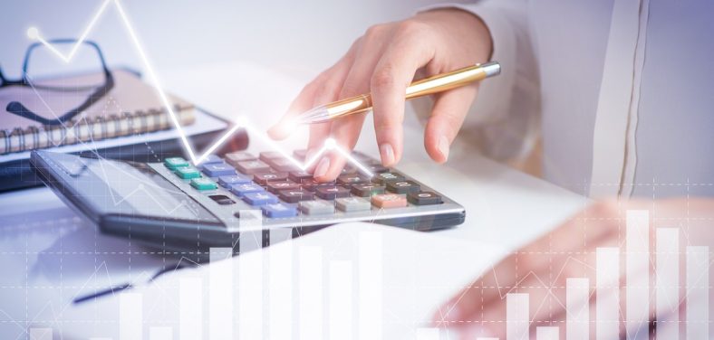 Accountant calculating profit with financial analysis graphs. Notebook, glasses and calculator lying on desk. Accountancy concept. Cropped view.